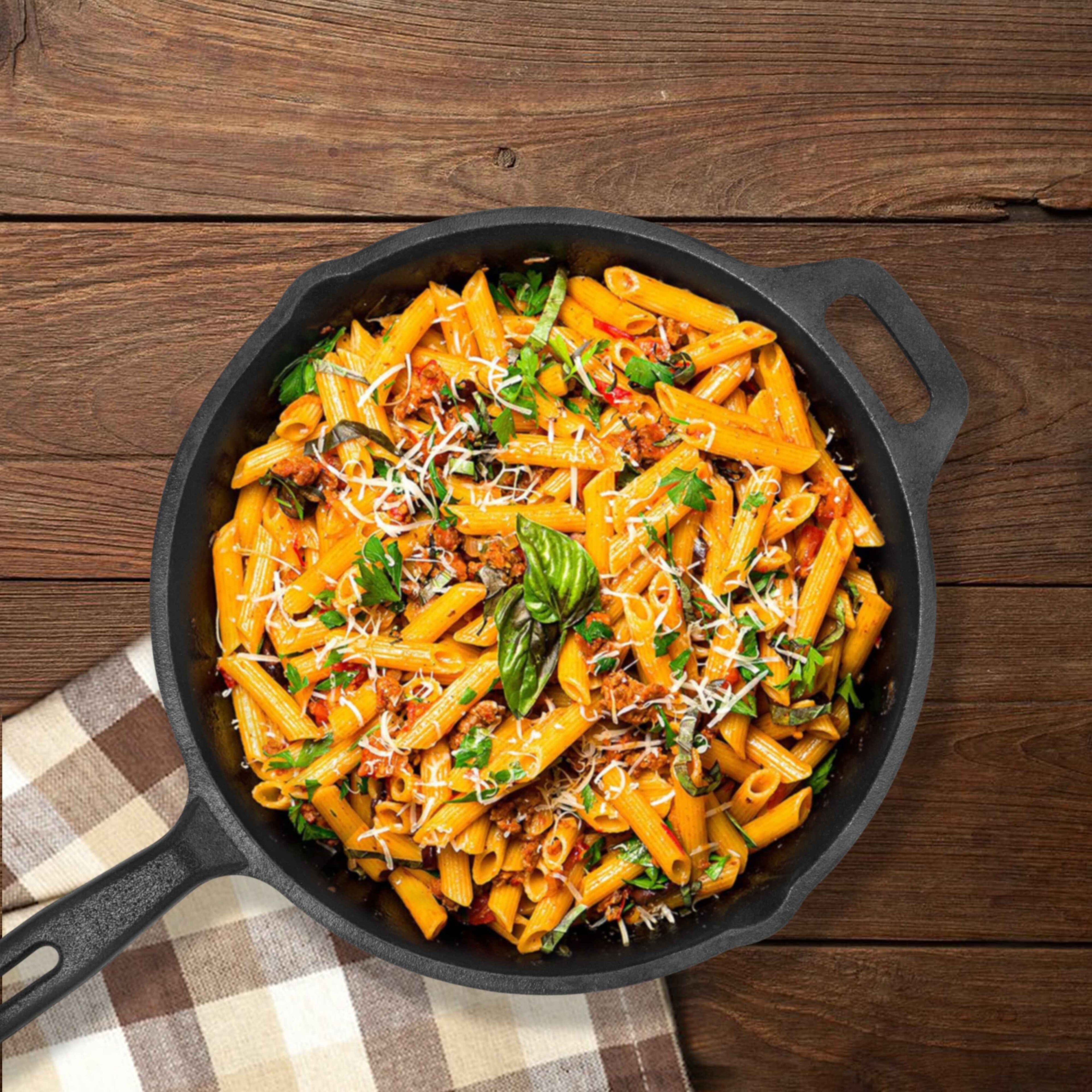 Penne pasta with tomato sauce, basil, and cheese in a black skillet on a wooden surface.