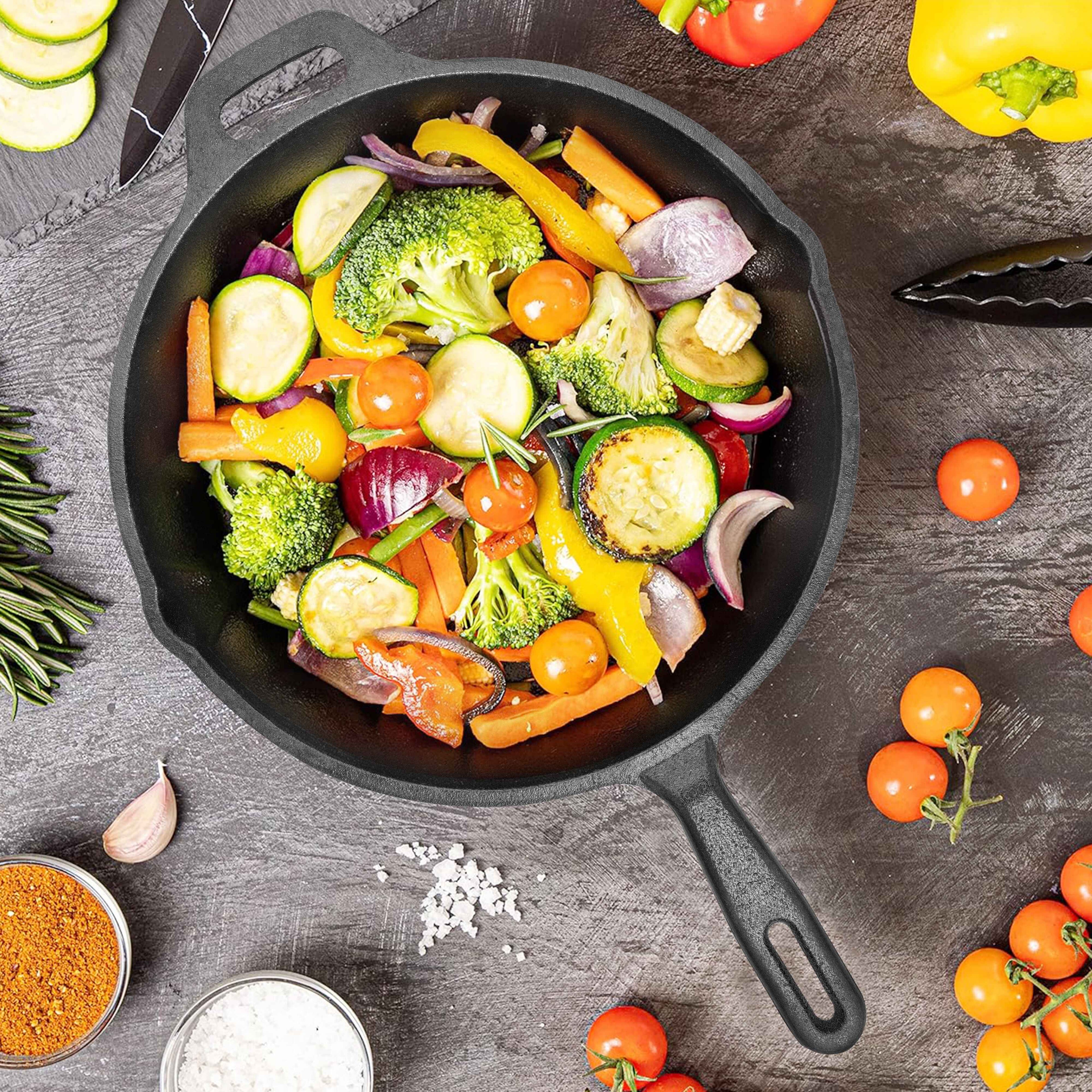 Fried vegetables in a black skillet on a wooden surface with additional vegetables around.